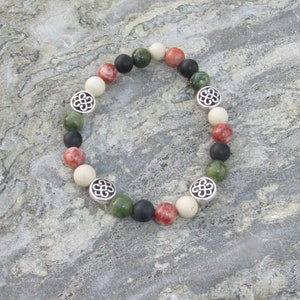 May include: A bracelet made of green, red, white, and black beads with silver charms. The charms are in the shape of a knot.