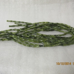 Op de afbeelding: Een streng groene jade kralen, elke kraal is gevormd als een bamboestok. De kralen zijn geregen op een wit draad.