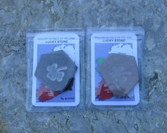 May include: Two small hexagonal shaped stones with a shamrock design carved into them. The stones are packaged in clear plastic bags with a card that says "Genuine Marble of Ireland Lucky Stone" and a map of Ireland. The cards are signed "by gerard".