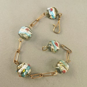 May include: A gold chain bracelet with five glass beads. The beads are clear with a silver and blue pattern and red accents.