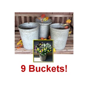 May include: Three galvanized metal buckets, each with a slightly different shape and size, are arranged on a wooden surface. The buckets are empty, but one is partially filled with fall leaves. The text "9 Buckets!" is printed below the buckets.