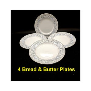 May include: Four white bread and butter plates with a blue and gray floral pattern. The plates are stacked on top of each other.