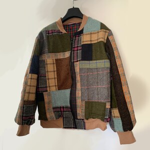 May include: A patchwork bomber jacket with a zip fastening. The jacket is made from different coloured fabrics with plaid patterns in shades of brown, green, blue and red.