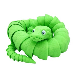 Op de afbeelding: Een groen slangen speelgoed gemaakt van zacht, flexibel materiaal. De slang is opgerold in een cirkel met zijn kop in het midden. De slang heeft grote, ronde ogen en een vriendelijke uitdrukking.