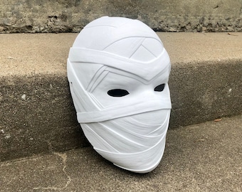Peut inclure: Masque en plastique blanc avec un design texturé ressemblant à un bandage. Le masque a deux trous pour les yeux et un nez large et plat.