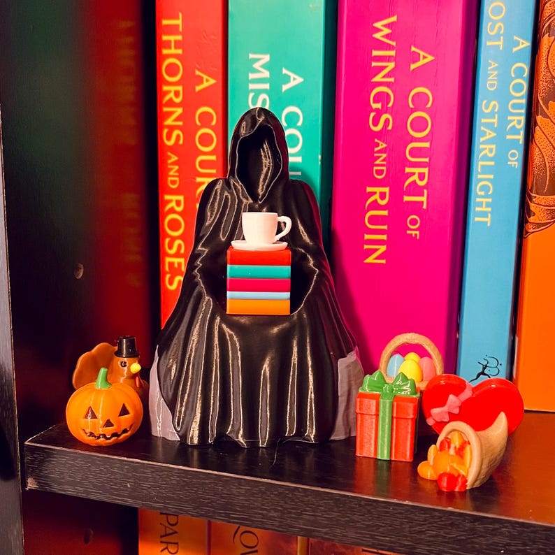 Op de afbeelding: Een zwarte figuur met capuchon die een stapel kleurrijke blokken vasthoudt met een kopje thee erop. Een pompoen, kalkoen, cadeau, hart en hoorn des overvloeds staan op een plank.