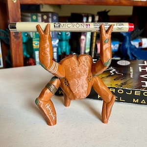 May include: A set of three ceramic mugs with a speckled, matte finish. The mugs are in shades of cream, light gray, and dark gray. Each mug has a simple, minimalist design and a rounded handle. The mugs are stacked on top of each other.