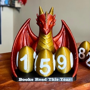 May include: A red and gold dragon-themed book counter with three golden egg-shaped number holders displaying the number 159. The base reads "Books Read This Year."