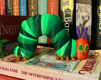 May include: A segmented caterpillar figurine featuring a curved body with alternating light and dark green sections, a bright orange head with yellow and green eyes, and two purple antennae. The figure has small brown feet along its underside.