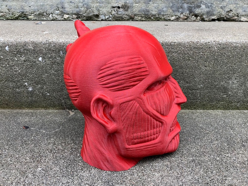 May include: A red 3D printed model of a human head with detailed muscle anatomy. The head is tilted to the side, and the mouth is slightly open.
