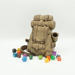 May include: A brown ceramic backpack with a rope handle and a small cup on the side. The backpack is surrounded by colorful dice.