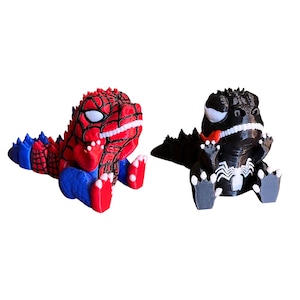 May include: Two 3D-printed figurines of cartoon dinosaurs. One is red, blue, and white, resembling Spider-Man. The other is black and white, with a red tongue, resembling Venom. Both are in a sitting position.