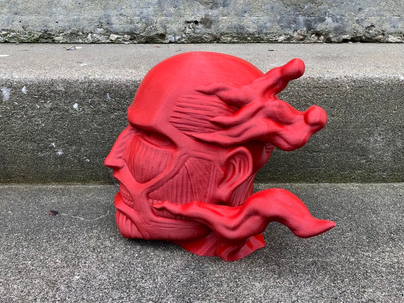May include: A red 3D printed sculpture of a human head with a detailed muscular structure and a flowing, flame-like design on the side.