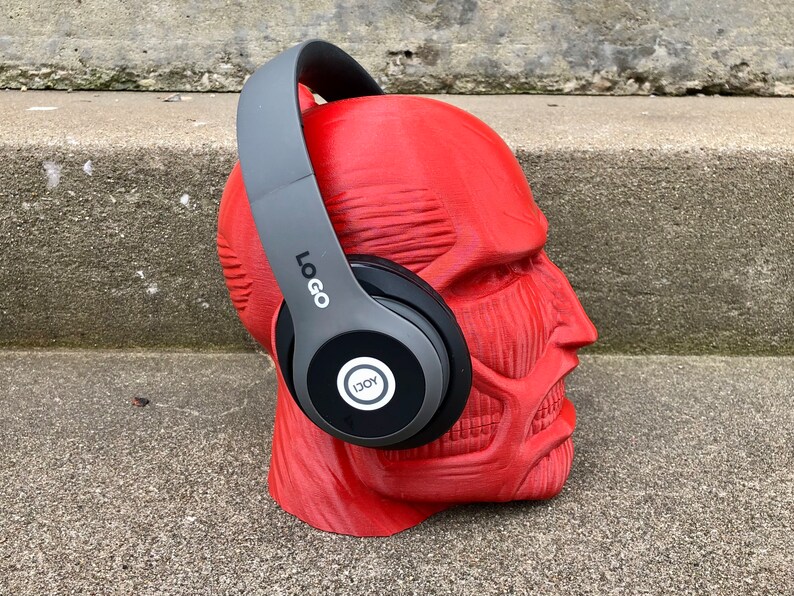 May include: Gray over-ear headphones with a black earcup featuring a white circle with the word "JOY" inside. The headphones are on a red mannequin head.