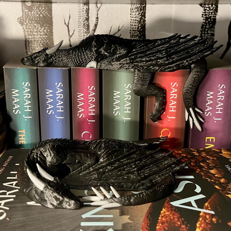 May include: Two black dragon bookends with white claws, resting on a stack of books with the title "SARAH J. MAAS" on the spines.