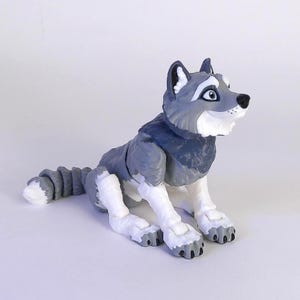 Puede incluir: Figura de lobo gris y blanco en posición sentada. El lobo tiene un diseño detallado con una cola esponjosa y una expresión amigable. La figura es un objeto decorativo.