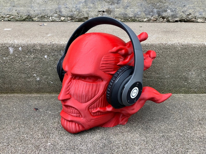 May include: A red 3D printed head sculpture of a character from the anime Attack on Titan wearing a pair of gray over-ear headphones.
