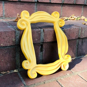 May include: A yellow plastic frame with a unique design, resembling a picture frame from the popular TV show "Friends".