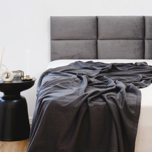 May include: A gray upholstered headboard with a tufted design, a gray blanket draped over a white bed, and a black side table with decorative items.