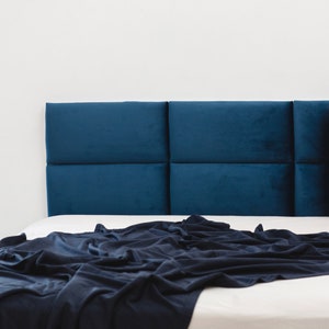 Könnte beinhalten: Ein blaues Samtkopfteil mit gestepptem Design. Das Kopfteil befindet sich auf einem weißen Bett mit einer dunkelblauen Decke.