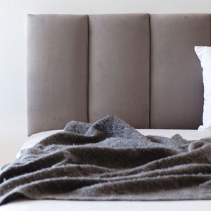 May include: A gray upholstered headboard with a gray blanket draped over it.