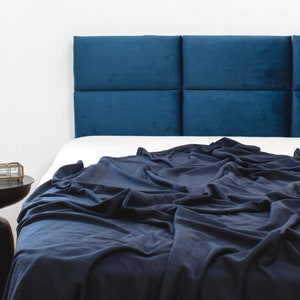 May include: A navy blue bed with a tufted headboard and a navy blue blanket. The headboard is made of multiple panels and is upholstered in a soft fabric.