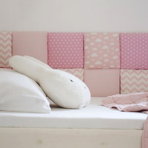 May include: A white bed with a pink and white patterned headboard. The bed is made with white sheets and a pink blanket. A white stuffed bunny is lying on the bed.