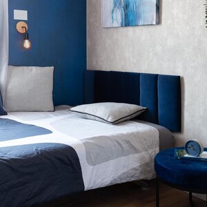 May include: A blue and white bed with a blue headboard and a white pillow. The bed is in a bedroom with a blue wall and a white wall.