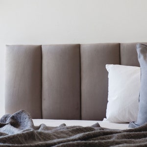 May include: A gray upholstered headboard with two pillows, one white and one gray, on a bed with a gray blanket.