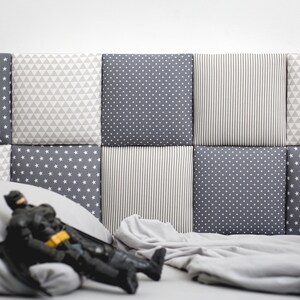 Puede incluir: Una cabecera con estampado gris y blanco con una colcha con estampado gris y blanco y una figura de acci&oacute;n negra tumbada en la cama.