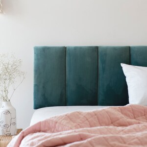 K&ouml;nnte beinhalten: Ein tealfarbenes Samtkopfteil mit einer rosafarbenen gesteppten Decke und wei&szlig;en und beigen Kissen auf einem Bett.