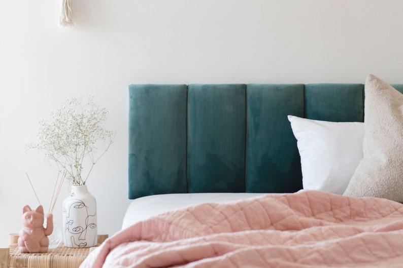K&ouml;nnte beinhalten: Ein tealfarbenes Samtkopfteil mit einer rosafarbenen gesteppten Decke und wei&szlig;en und beigen Kissen auf einem Bett.