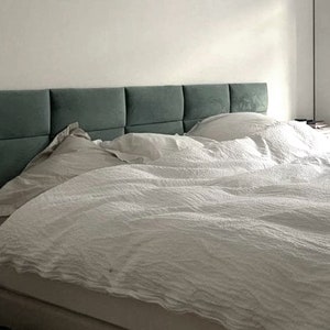 May include: A white bed with a teal headboard and white bedding. The headboard is made of multiple panels.