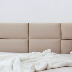 May include: A white bed with a beige headboard and a white blanket. The headboard is made of multiple panels.