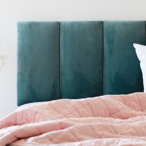Puede incluir: Una cabecera de terciopelo azul verdoso con tres paneles, un edredón acolchado rosa y una almohada blanca.
