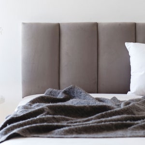 May include: A gray upholstered headboard with a tufted design. A gray blanket is draped over the bed, and a white pillow is on the bed.