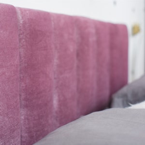 K&ouml;nnte beinhalten: Nahaufnahme eines rosafarbenen Samtkopfteils mit einer gesteppten Gestaltung. Das Kopfteil ist Teil eines Bettes mit grauer Bettw&auml;sche.