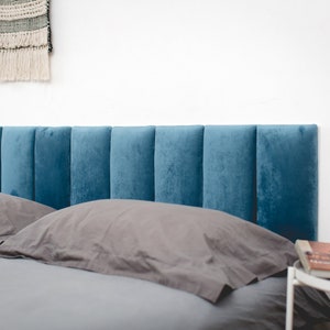 May include: A teal blue upholstered headboard with vertical panels. The headboard is on a bed with grey and white bedding.