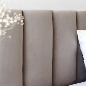 May include: A close-up of a grey upholstered headboard with vertical channel tufting. The headboard is part of a bed with a white pillow on top.