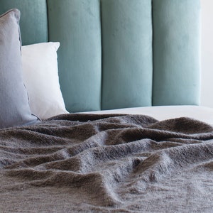 May include: A gray throw blanket is draped over a bed with a teal headboard. The blanket is wrinkled and has a soft, fuzzy texture.