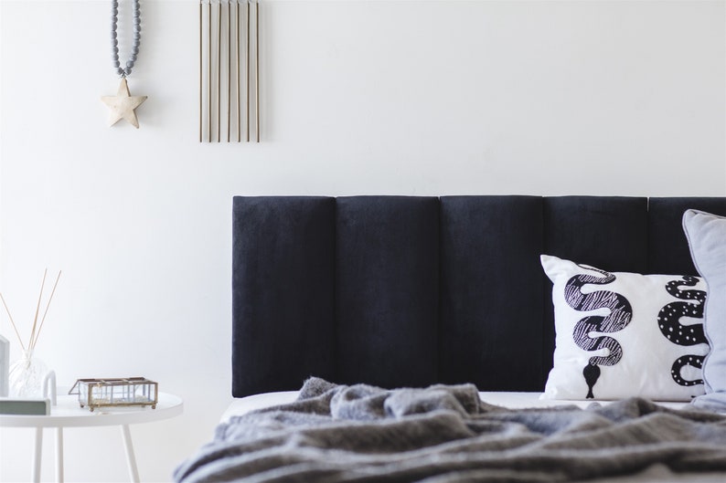 K&ouml;nnte beinhalten: Ein schwarzes, gestepptes Kopfteil mit einem wei&szlig;en Kissen mit einem schwarzen Schlangenmuster. Eine graue Decke liegt &uuml;ber dem Bett.
