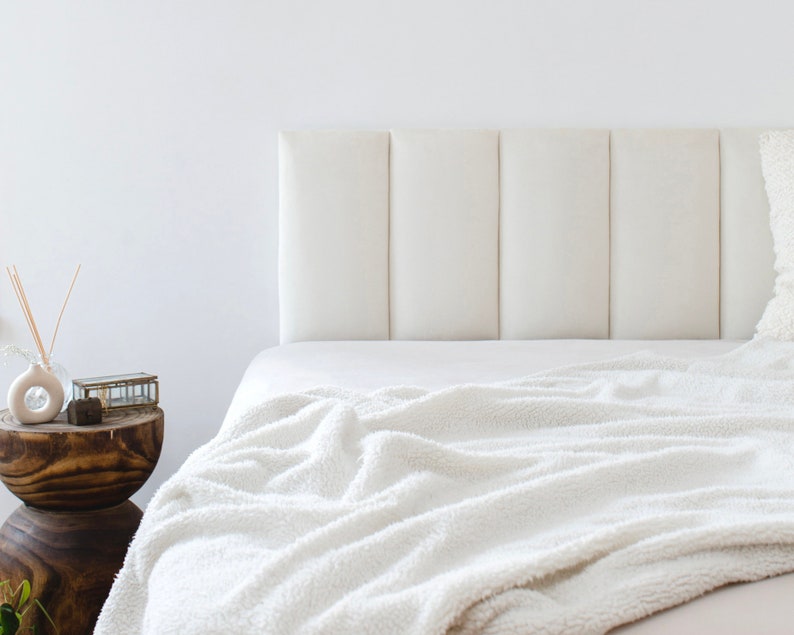K&ouml;nnte beinhalten: Ein wei&szlig;es, gepolstertes Kopfteil mit einem gesteppten Design. Das Bett ist mit wei&szlig;er Bettw&auml;sche und einer flauschigen wei&szlig;en Decke bezogen.