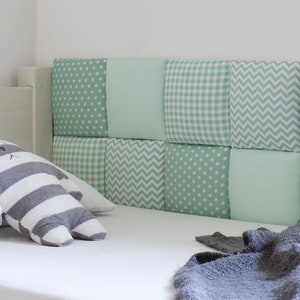 May include: A white bed with a green and white patterned headboard. The headboard is made of individual squares of fabric with different patterns. A gray and white striped stuffed animal is on the bed.