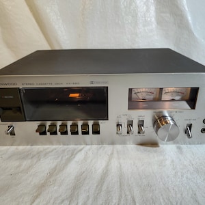 May include: A silver Kenwood KX-620 stereo cassette deck. The deck features a cassette slot, VU meters, and various control knobs and buttons. The unit has a black top and a brushed metal faceplate.