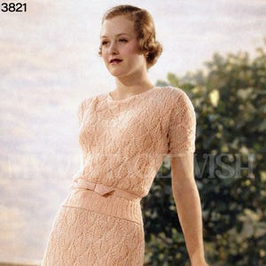 Puede incluir: Un vestido de encaje de dos piezas color melocotón vintage de la década de 1930. El vestido presenta una parte superior de manga corta con cuello redondo y una falda lápiz a juego. Un cinturón de lazo ciñe la cintura. El vestido está hecho de una tela delicada y de tejido abierto.