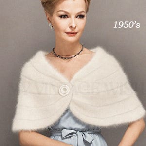 May include: A vintage-style image featuring a woman in a light blue dress and a cream-colored, fluffy shawl. The shawl is fastened with a round button. The image has the text "1950's" and "717" in the upper left corner.