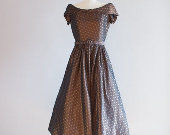 May include: A brown and gold polka dot dress with a fitted bodice and a full skirt. The dress has a brown belt and short sleeves.