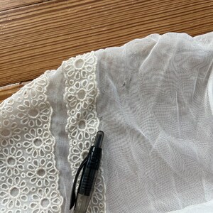 Pode incluir: Tecido branco transparente com uma borda de renda branca. Uma caneta preta est&aacute; sobre o tecido.