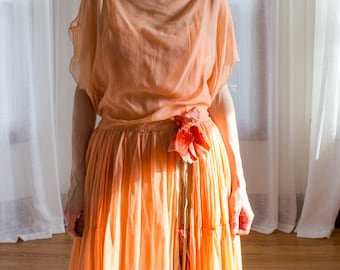 May include: A peach-coloured sheer dress with a flowing skirt and a flower detail at the waist.