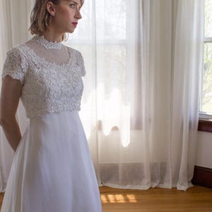 May include: A white lace wedding dress with a high neckline and short sleeves. The dress has a full skirt and is made of a soft, flowing fabric.